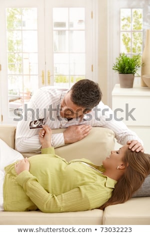 Stockfoto: Pregnant Woman Looking At Her Babys Ultrasound Scan In Her Living Room