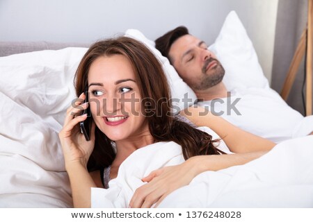 Zdjęcia stock: Woman Talking On Smartphone Besides Her Husband Sleeping On Bed