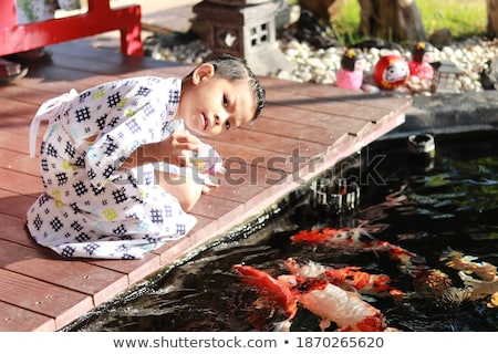 [[stock_photo]]: Young Boy Feeding Koi Fish With Milk Bottle