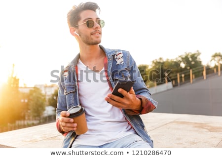 Foto stock: Handsome Young Guy Walking Outdoors Using Mobile Phone Drinking Coffee Listening Music