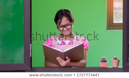 Foto d'archivio: Black Hair Little Girl With Glasses Holding Books By The Wall