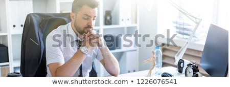 Foto stock: A Man Is Sitting At A Table In The Office And Is Looking At A Wooden Little Man