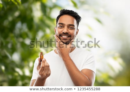 [[stock_photo]]: Smiling Indian Man Applying Grooming Oil To Beard