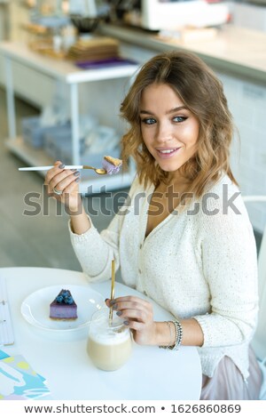[[stock_photo]]: Young Smiling Female Having Nice Time In Cafeteria While Eating Cheesecake