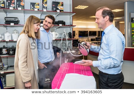 商業照片: Salesman Showing Steam Iron To Couple In Hypermarket