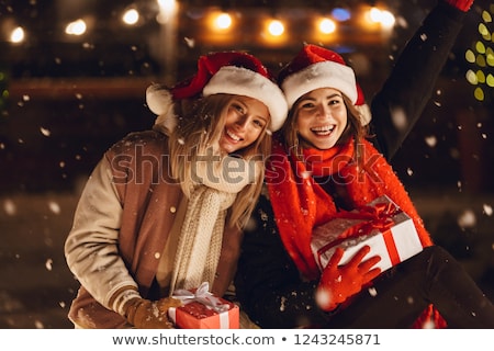 Foto d'archivio: Happy Young Friends Sitting Outdoors In Evening In Christmas Hats Holding Gift Box