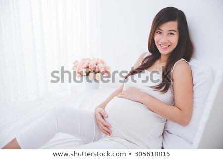 Foto d'archivio: Happy Asian Pregnant Woman With Flowers In Bed