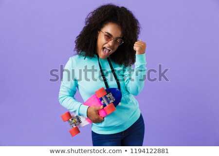 Foto stock: African Girl Posing Isolated Over Violet Background Holding Skateboard Showing Winner Gesture