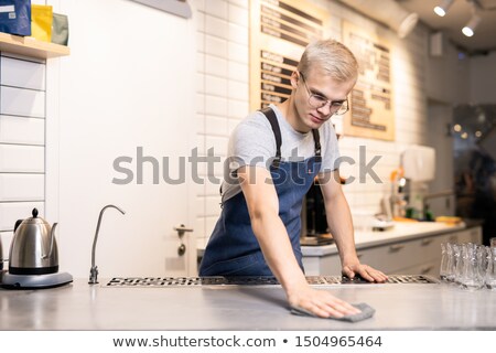 Stockfoto: Young Barista Or Waiter In Workwear Wiping His Workplace With Wet Duster