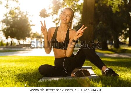 Stok fotoğraf: Blonde Sports Woman In Park Outdoors Listening Music Wth Earphones Showing Peace Gesture