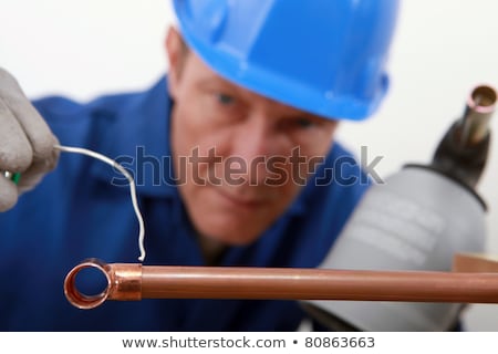 Foto stock: Skilled Tradesman In Blue Jumpsuite Is Soldering A Copper Pipe