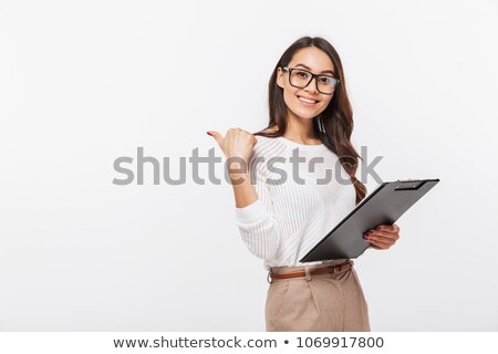 [[stock_photo]]: Smiling Attractive Young Businesswoman Holding Clipboard And Pointing Away