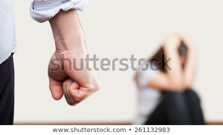 Foto d'archivio: Angry Man Raised Fist Over Wall Corner Sitting Woman