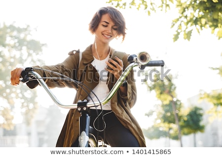 [[stock_photo]]: Cute Young Woman Walking In Park With Bicycle Listening Music With Earphones
