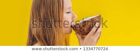 Stockfoto: Young Woman Drinking Coconut Milk On Chafrom Coconut On A Yellow Background Banner Long Format