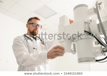 Foto d'archivio: Bearded Young Man In Whitecoat And Eyeglasses Tuning And Checking Equipment