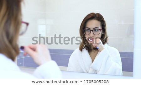 Stok fotoğraf: Pretty Female Brushing Her Teeth In Front Of Mirror