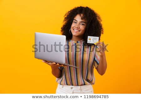 Stockfoto: Emotional African Woman Posing Isolated Over Yellow Background Using Laptop Computer Holding Credit