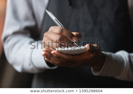 Foto stock: Young Waiter Or Worker Of Cafeteria Writing Down Orders Of Clients In Notepad
