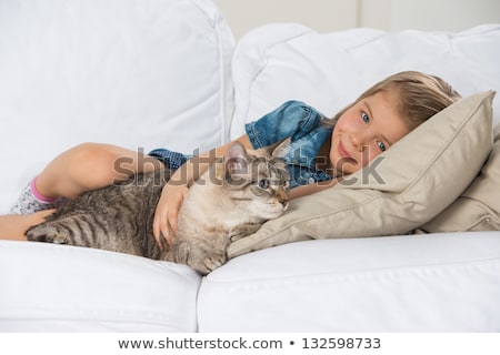 [[stock_photo]]: Little Girl Laying On Sofa With Her Tabby Cat