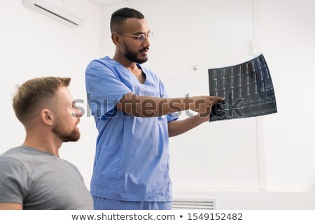 Сток-фото: Radiologist In Uniform Pointing At One Of Fragments On X Ray Of Broken Joint