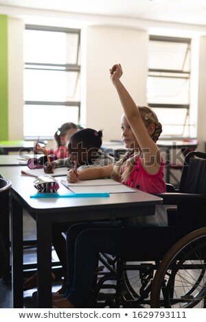 Stock foto: Side View Of Disable Schoolgirl Raising Hand And Sitting At Desk In Classroom Of Elementary School