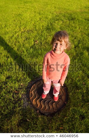 Stok fotoğraf: Girl Is Standing On Hatch In Grass Smiling Little Girl View From Above Water Drain Rusty Hatch On