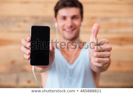 Stockfoto: Man Holding Smartphone With Headphones And Showing Thumb Up