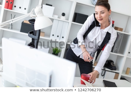 Foto d'archivio: A Young Girl Stands In The Office Near A Computer Desk And Holds A Red Cup In Her Hands