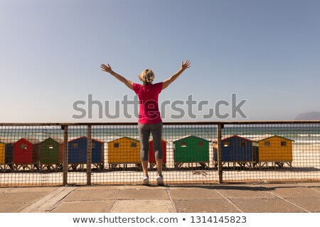 ストックフォト: Rear View Of Senior Woman Standing With Arms Outstretched On A Promenade At Beach