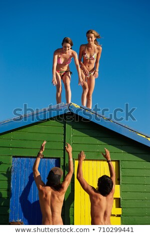 Foto stock: Girls About To Climb Off Beach Hut Roof