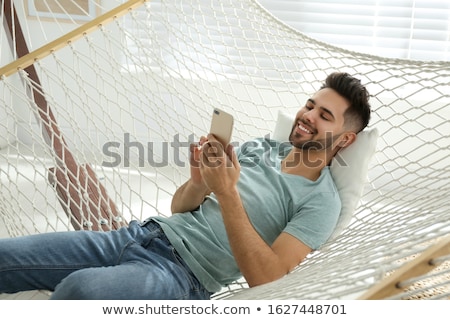 Foto stock: Happy Man Using Smartphone In Hammock