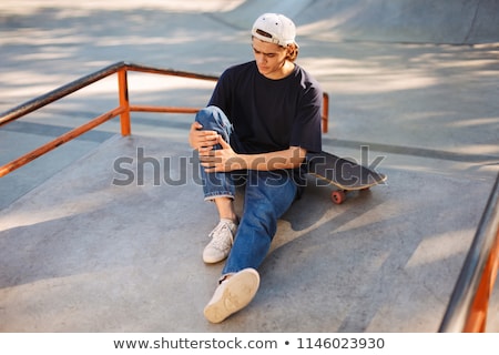 Foto stock: Young Skater Guy Sit In The Park With Skateboard