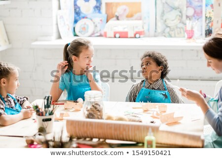 Foto stock: Cute Multicultural Schoolkids Sitting By Desk At Lesson And Discussing Ideas