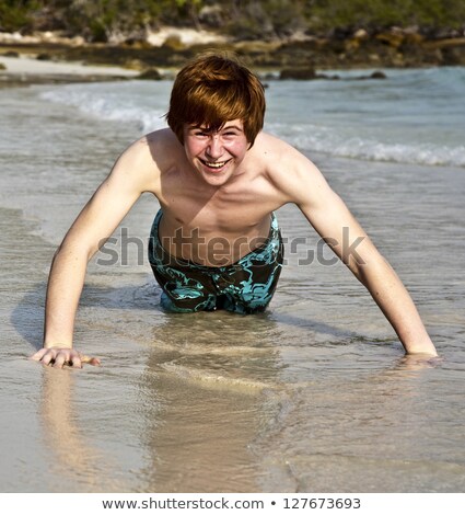 Stock photo: Boy In Bathingsuit Is Lying At The Beach And Enjoying The Saltwater With Tiny Waves And Smiles