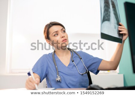 Stockfoto: Young Brunette Female Radiologist Looking At X Ray Result Of One Of Patients