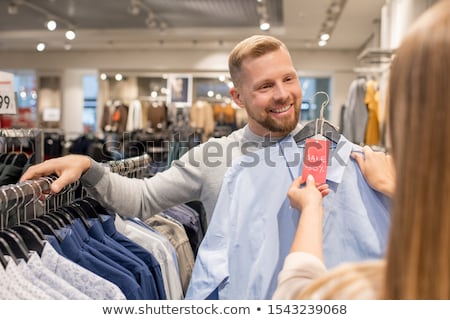 Stok fotoğraf: Happy Young Man Showing His Girlfriend Blue Shirt With Fifty Percent Discount