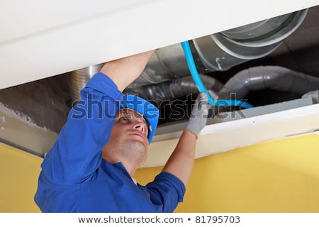 商業照片: Worker Holding Blue Pipe In Place Under Air Ducts