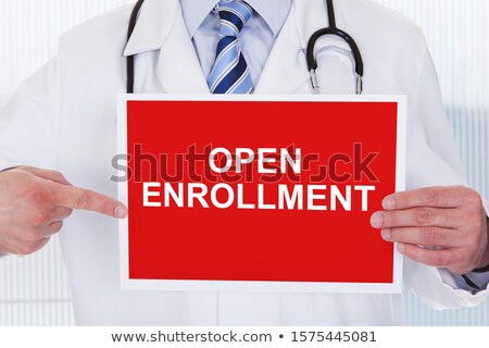 Stockfoto: Male Doctor Pointing At Open Enrollment Placard Holding In Hand
