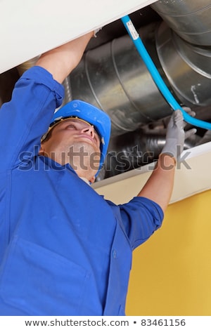 Stock fotó: Plumber Holding A Blue Flexible Pipe Under Some Air Ducts