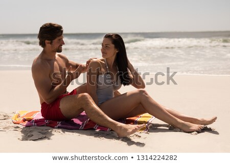[[stock_photo]]: Side View Of Happy Young Man Applying Sunscreen Lotion On Woman Back At Beach In The Sunshine