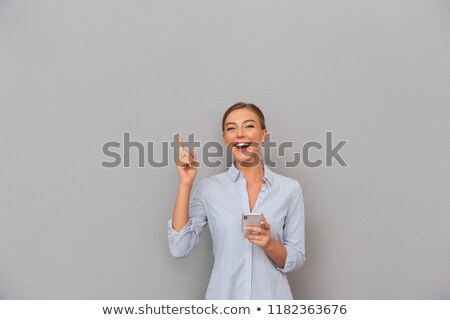 Stockfoto: Beautiful Smiling Business Woman Standing Over Grey Wall Background Using Mobile Phone Pointing