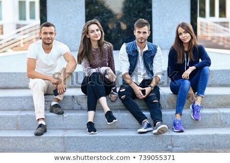 Stockfoto: Happy Young Man Sitting On Steps Outdoors Looking Camera Holding Phone