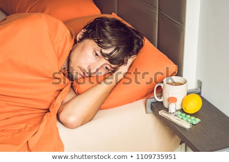 Foto stock: Man Feeling Cold Lying In The Bed And Drinks Tea And Measures Temperature With A Thermometer