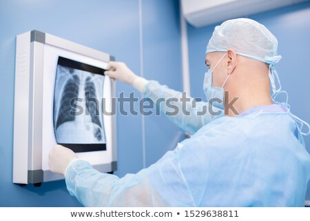 ストックフォト: Experienced Professional In Surgical Uniform And Mask Looking At Lungs X Ray