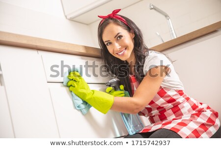 Stock foto: Lovely Young Housemaid In Apron Cleaning White Kitchen Cupboard