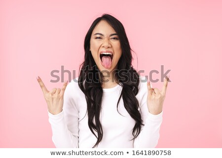 Foto d'archivio: Image Of Young Asian Woman Having Fun And Gesturing Horn Fingers