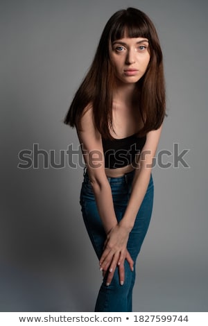 Foto stock: Young Beautiful Brunette Woman In Black Top And Jeans Isolated On Grey Background