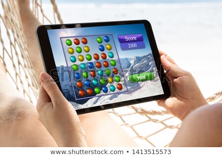 Stockfoto: Woman Lying On Hammock Playing Video Game On Digital Tablet