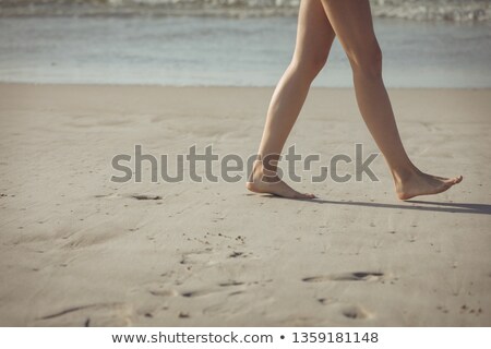 [[stock_photo]]: Low Section Of Young Caucasian Woman Walking On The Sand With Barefoot At Beach On Sunny Day